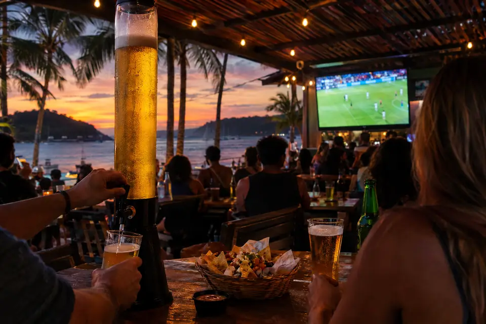 A beer tower pouring at the table with nachos at sunset, the game on the screen behind